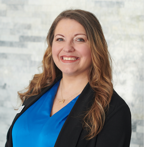 Smiling woman in a blue blouse and black blazer against a light background