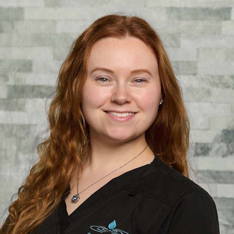 Smiling red-haired person in a black shirt against a gray brick wall background