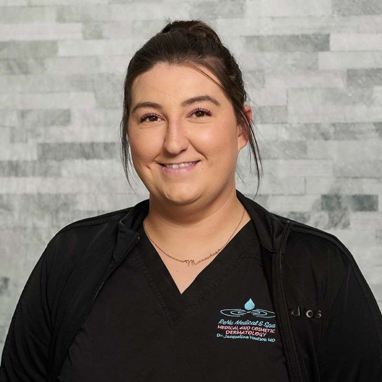 Smiling person in a black uniform standing against a gray tiled wall