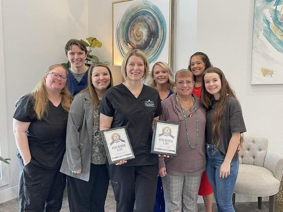 Group posing indoors with framed awards, smiling in front of wall art