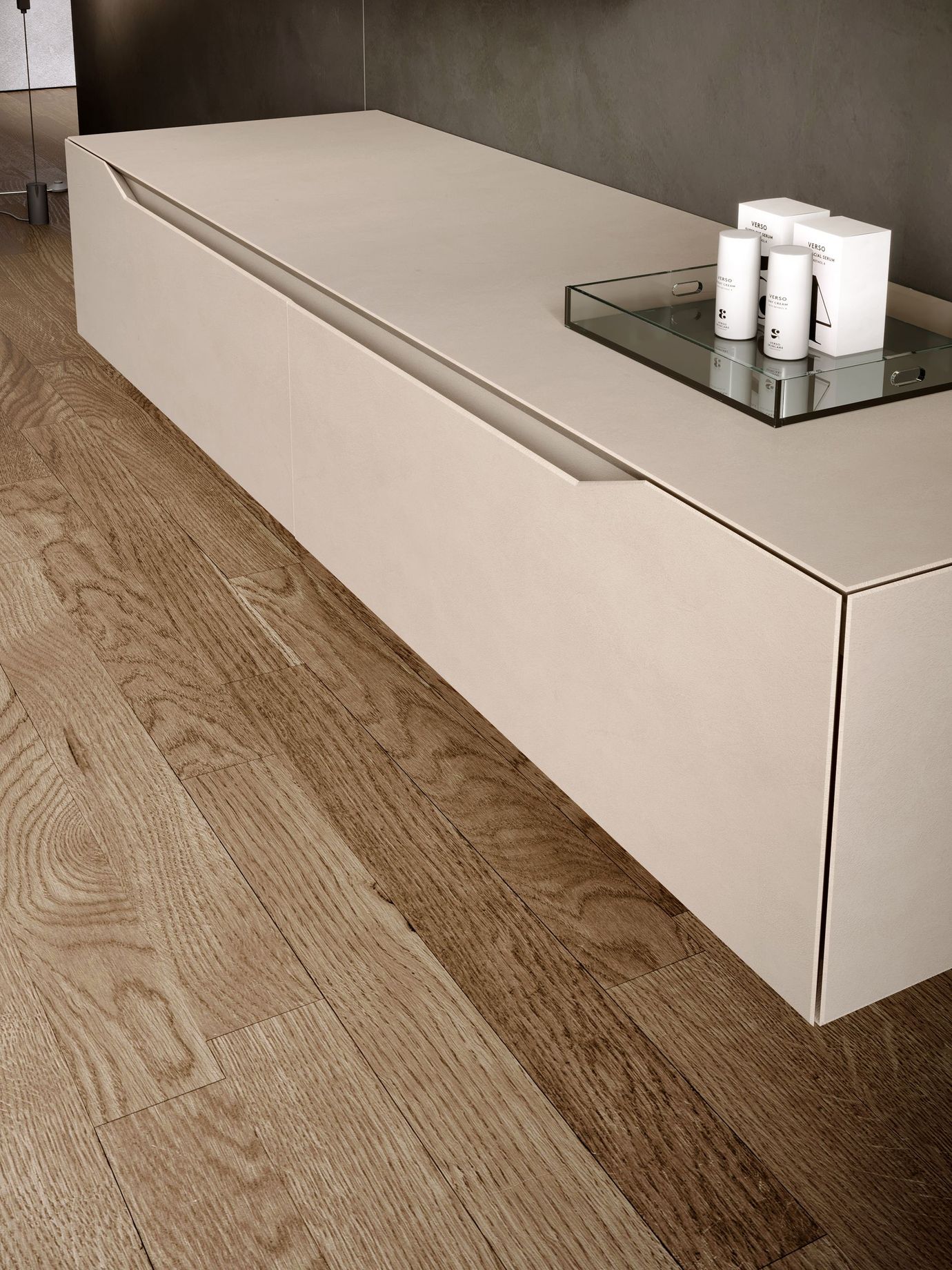 Bagno moderno con un lungo lavandino bianco rettangolare e rubinetti cromati. Divano grigio vicino a una finestra con vegetazione.
