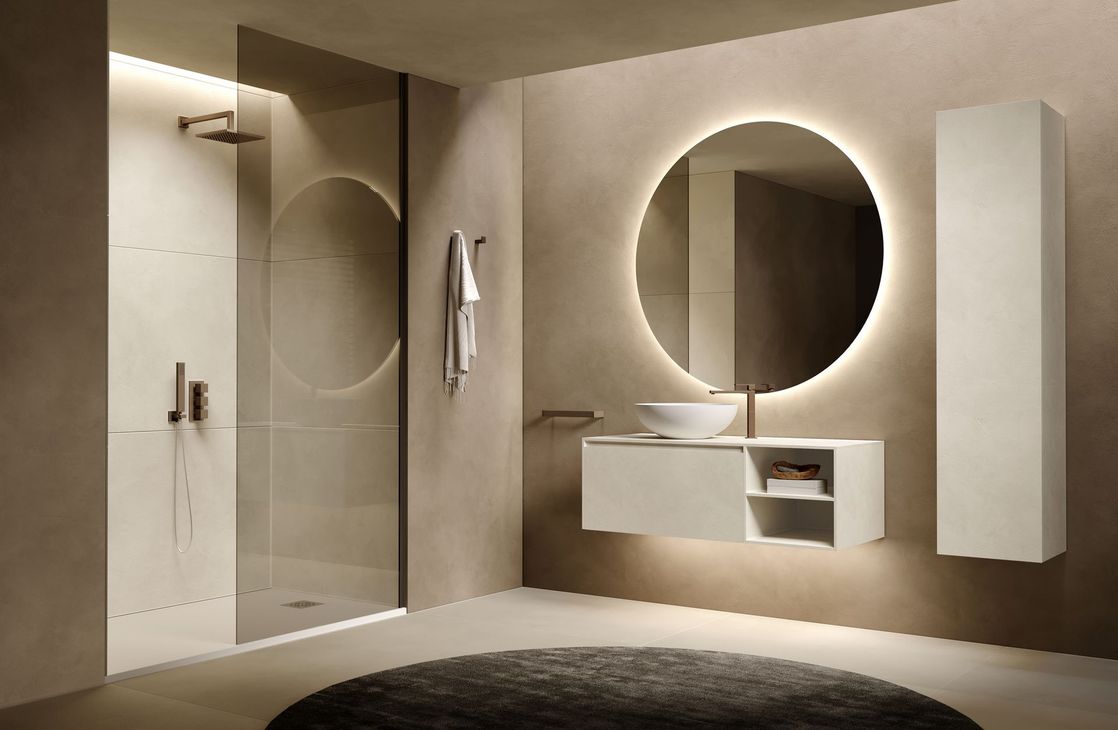 Bagno moderno con specchio rotondo retroilluminato, mobile lavabo bianco, doccia e tappeto rotondo.