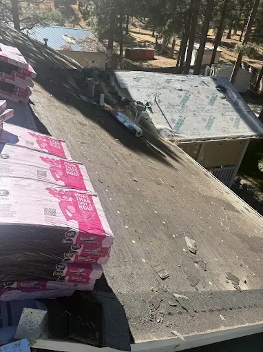 Construction materials stacked on a rooftop beside a sloped concrete roof and trees below.