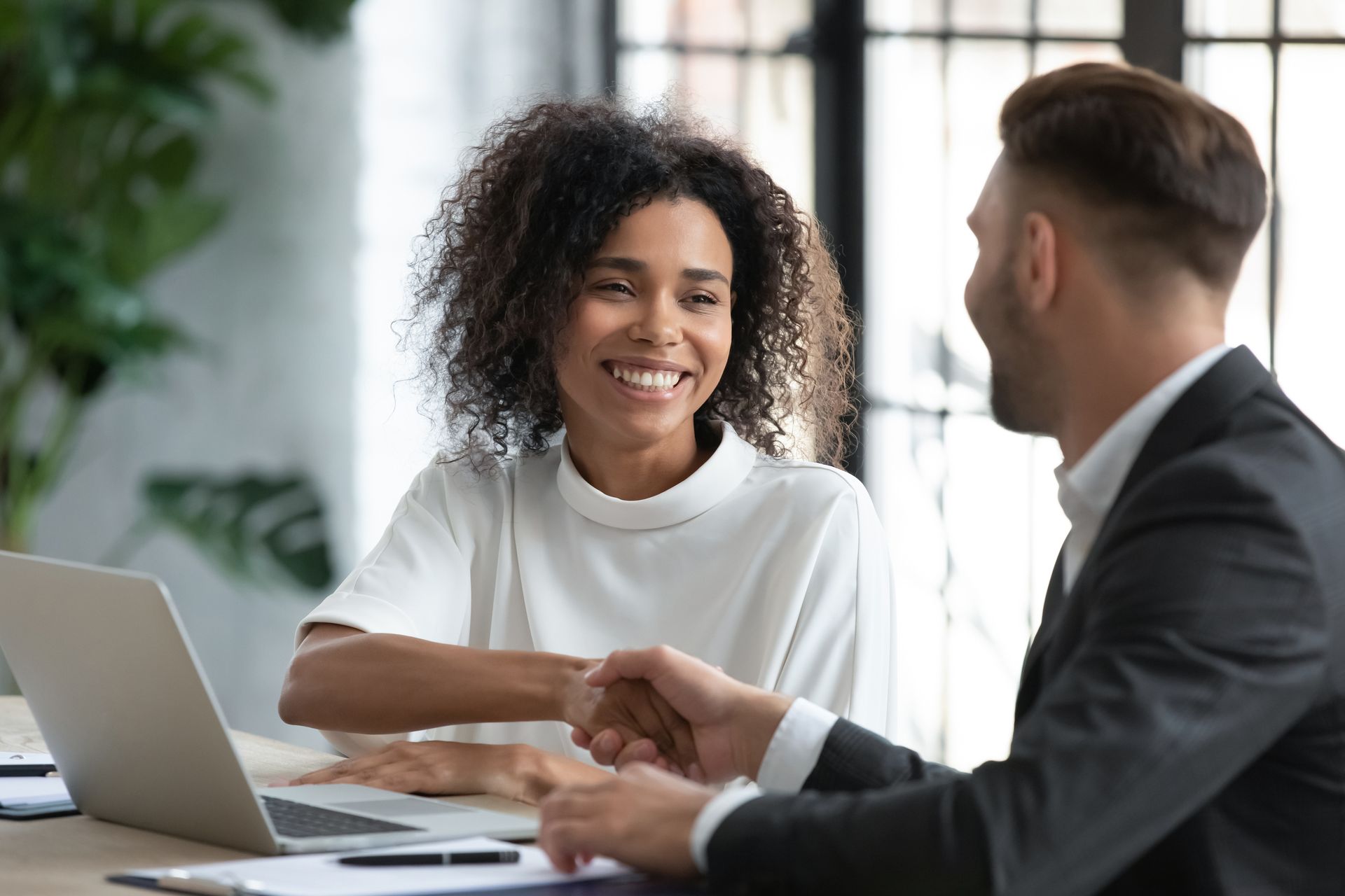A man and woman shaking hands in front of a laptop.