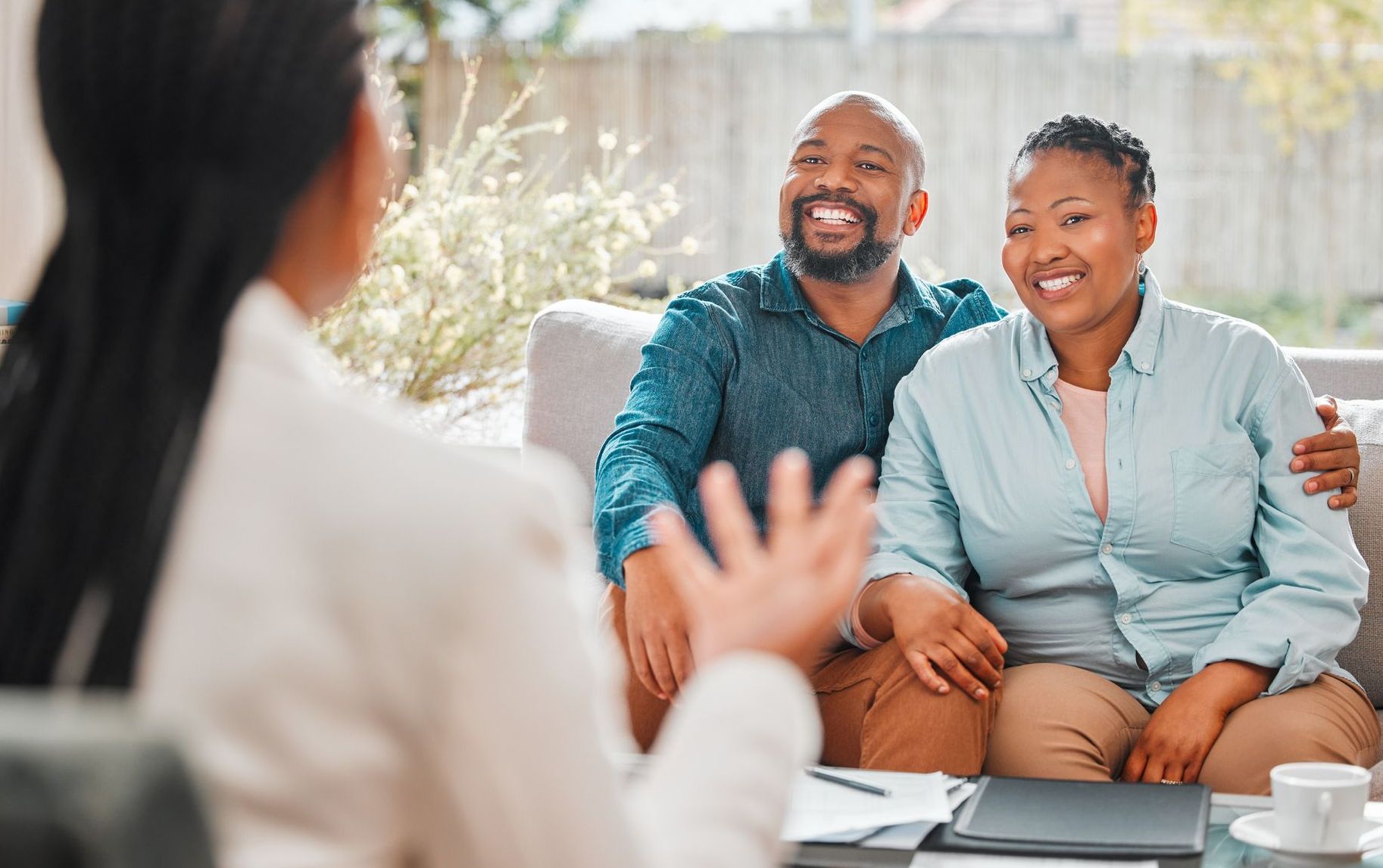 A man and woman sit on a couch while speaking to a woman.
