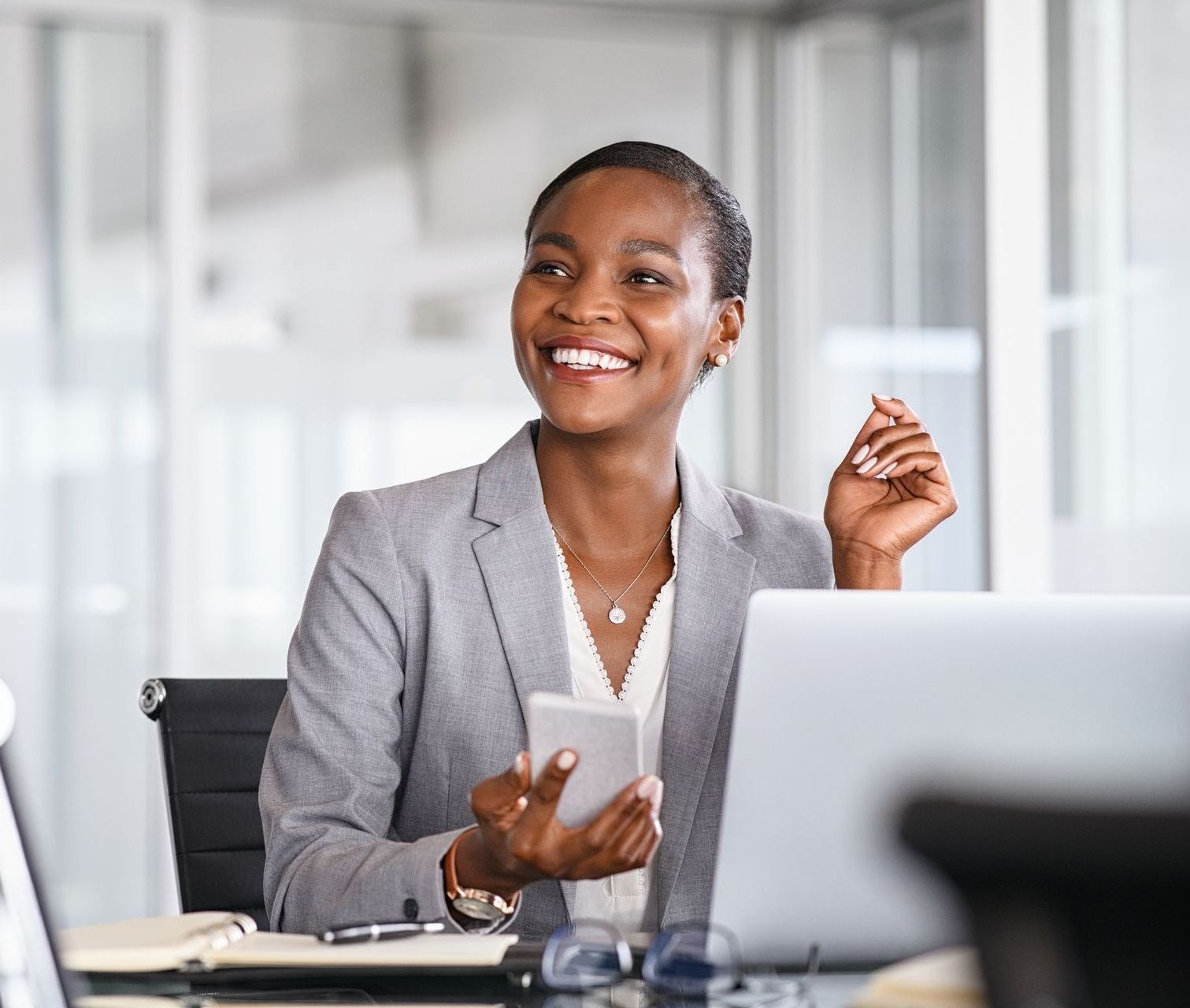 A woman sitting at a desk holding a tablet and smiling.