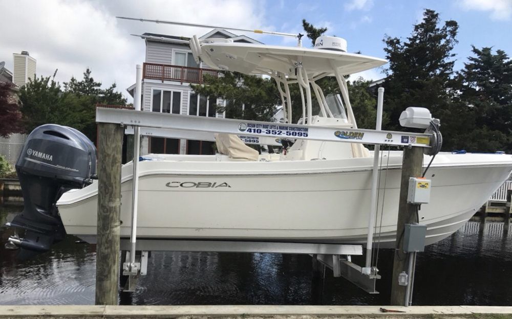 A white boat is sitting on a lift next to a house.