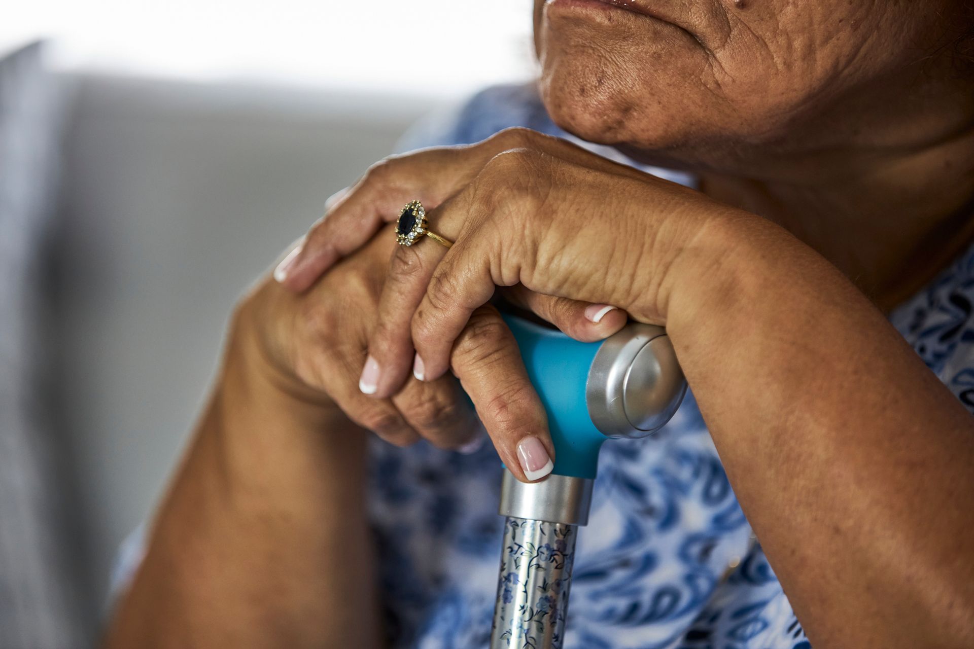 Elderly person resting hands on a cane with a ring on one finger.