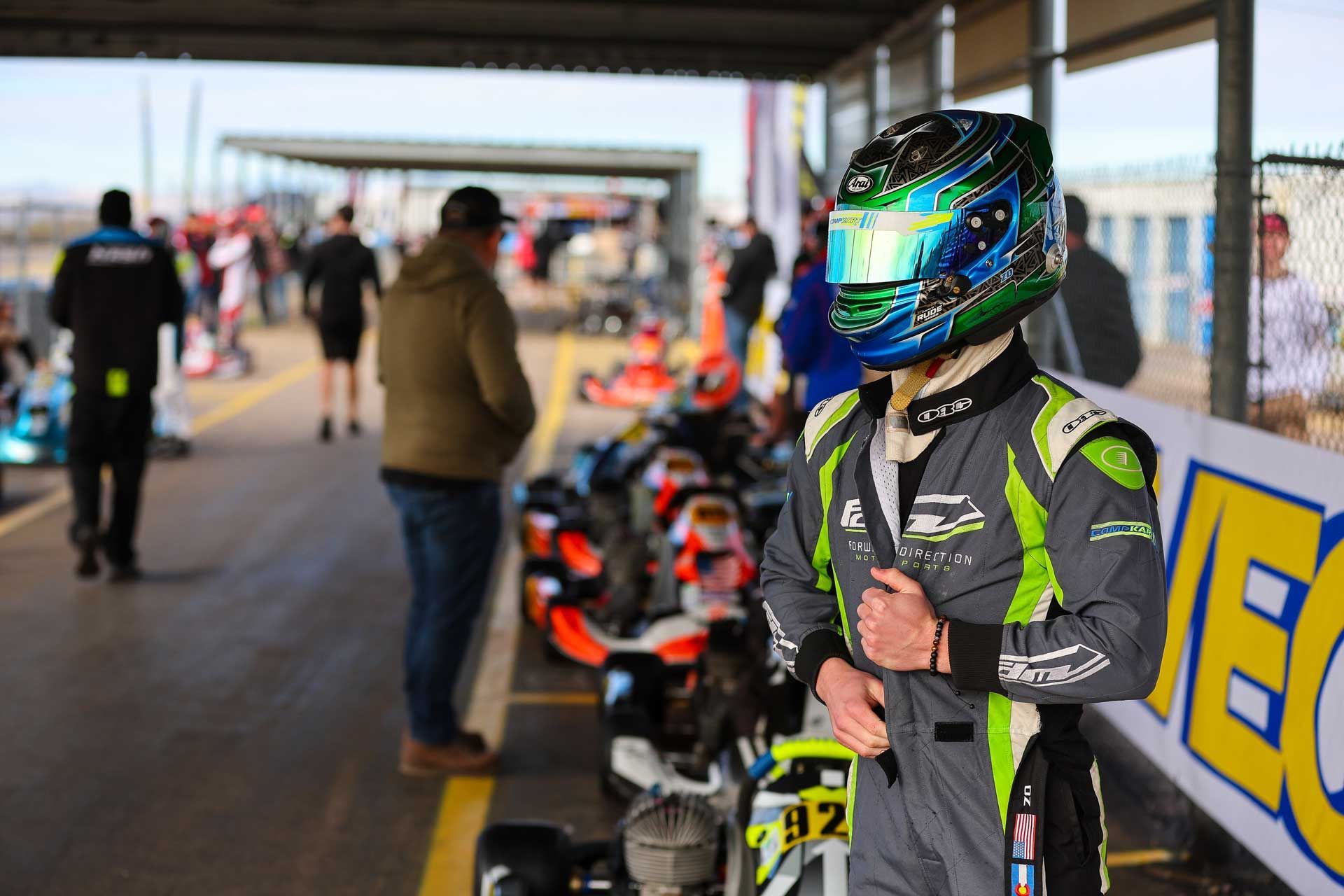 A man wearing a helmet is standing next to a row of go karts.