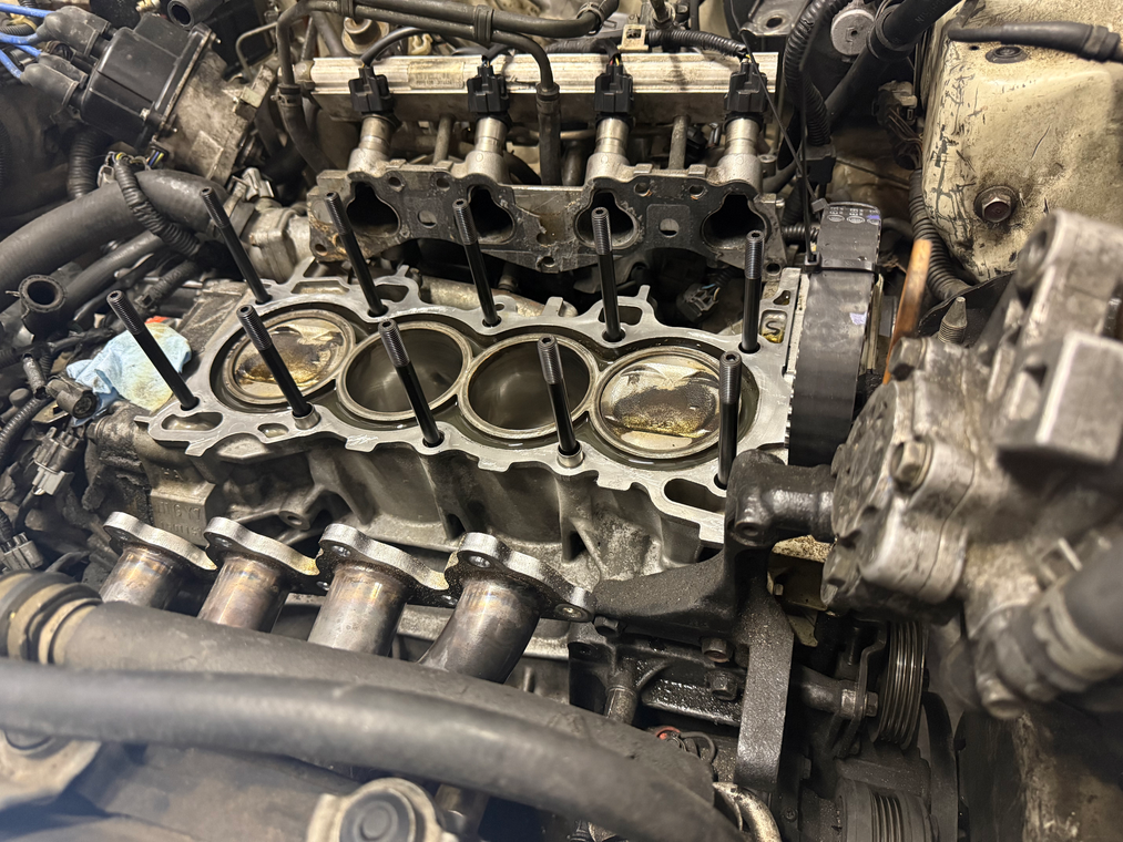 Close-up of a disassembled engine block with exposed pistons and hoses in a repair shop.