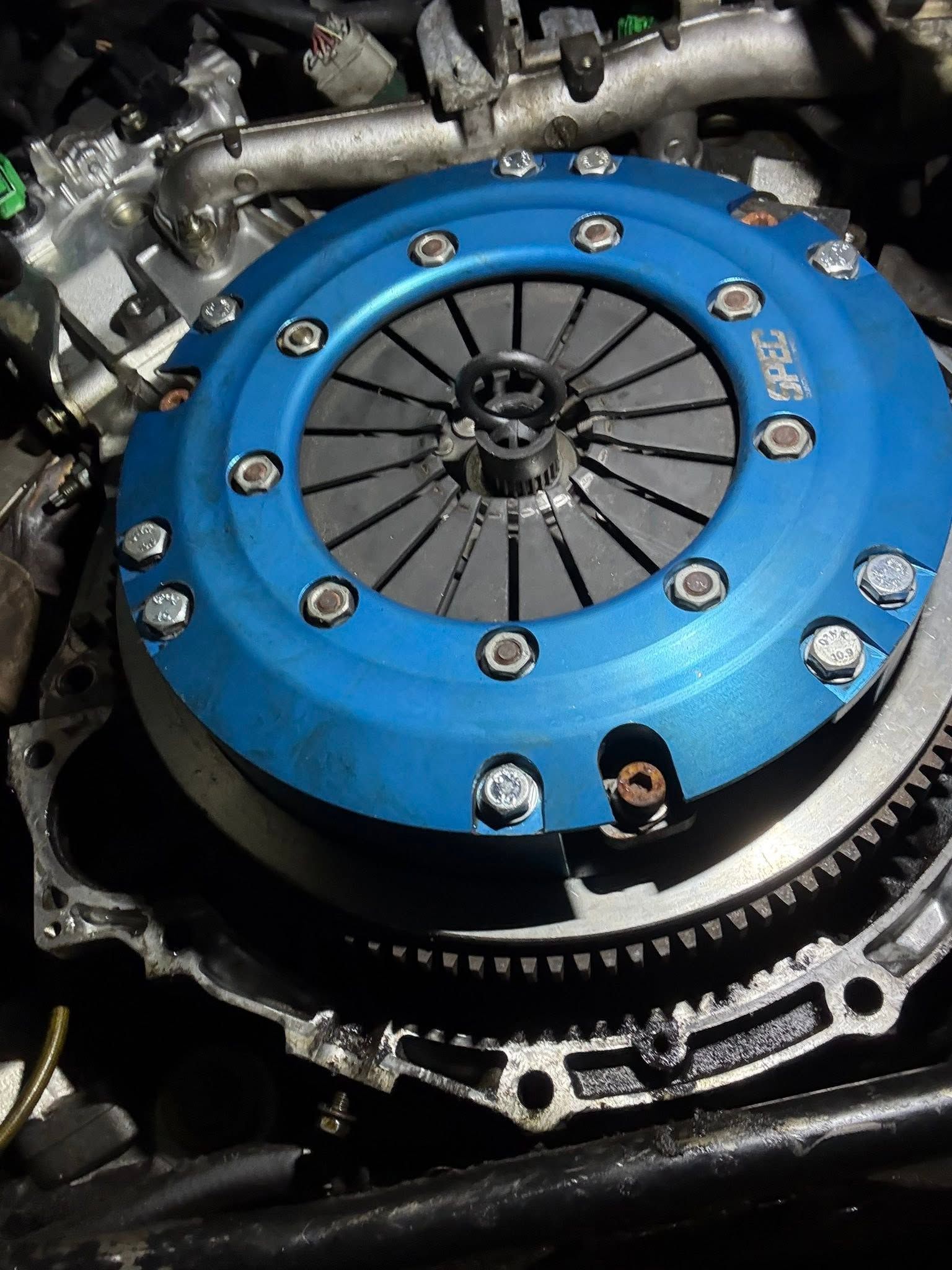 Blue performance clutch assembly inside an engine bay, with bolts and black pressure plate visible
