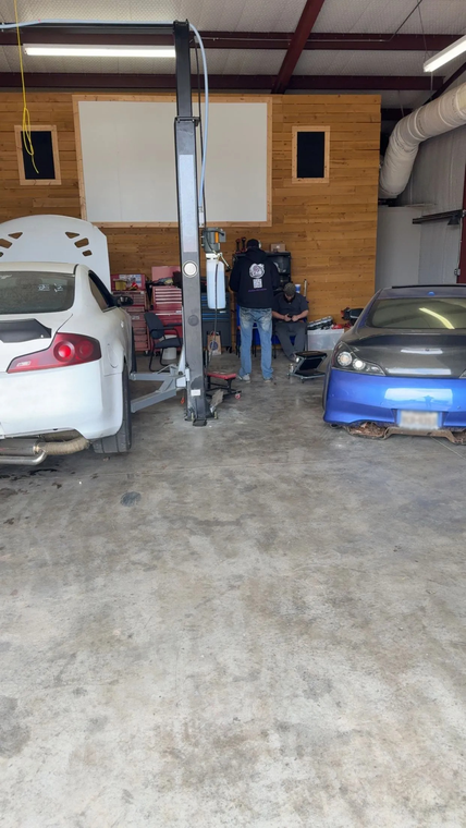 Auto repair garage with a silver sedan, blue car, and two people near a vehicle lift