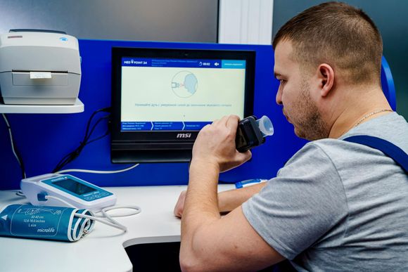 A man is sitting at a desk using a breath test machine.