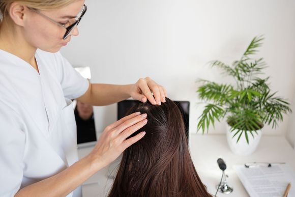 A woman is examining a woman 's hair in a doctor 's office.