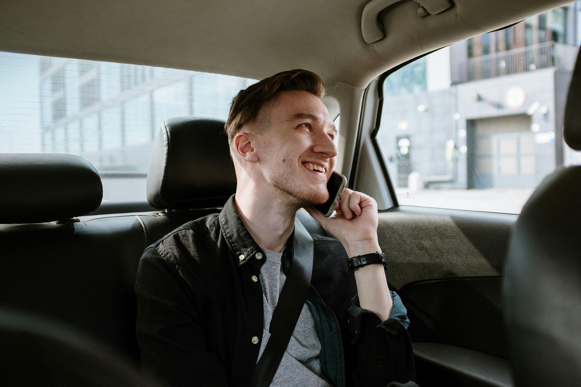 A man is sitting in the back seat of a car talking on a cell phone.