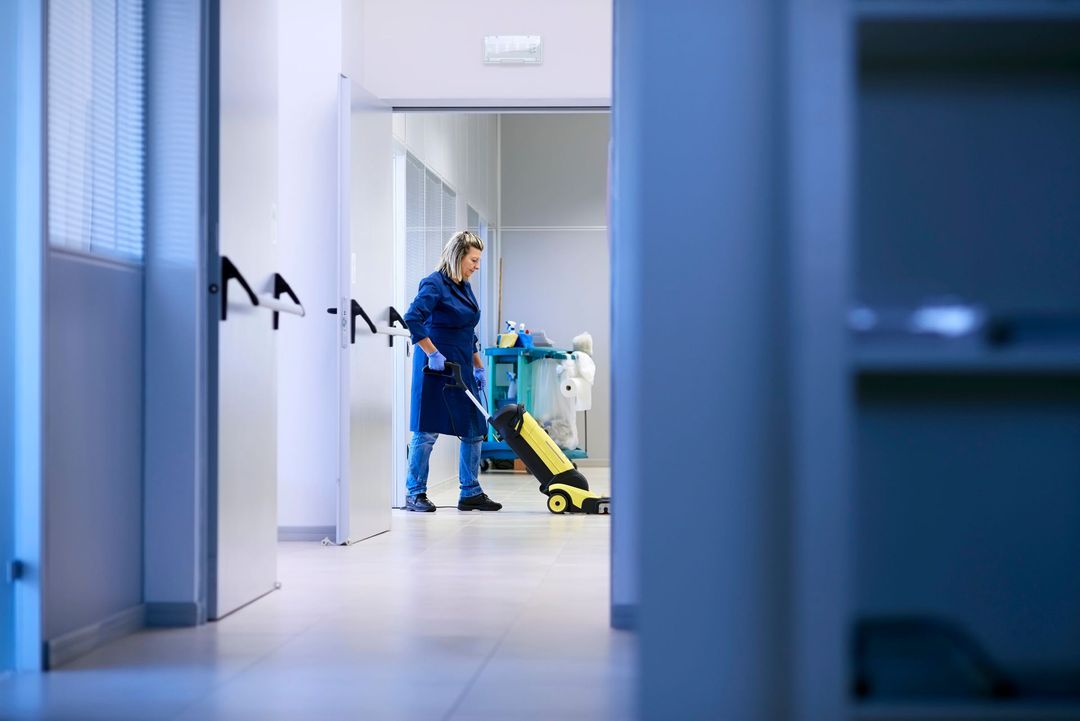 Una persona che indossa guanti blu sta pulendo il pavimento con un panno e uno spruzzatore.