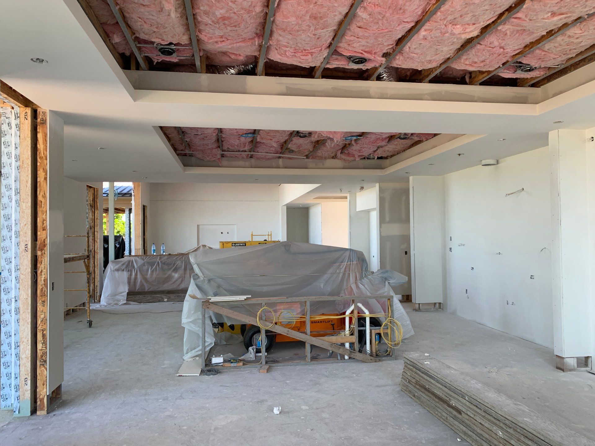 An empty room with a couch and a ladder in it and drywall being installed.