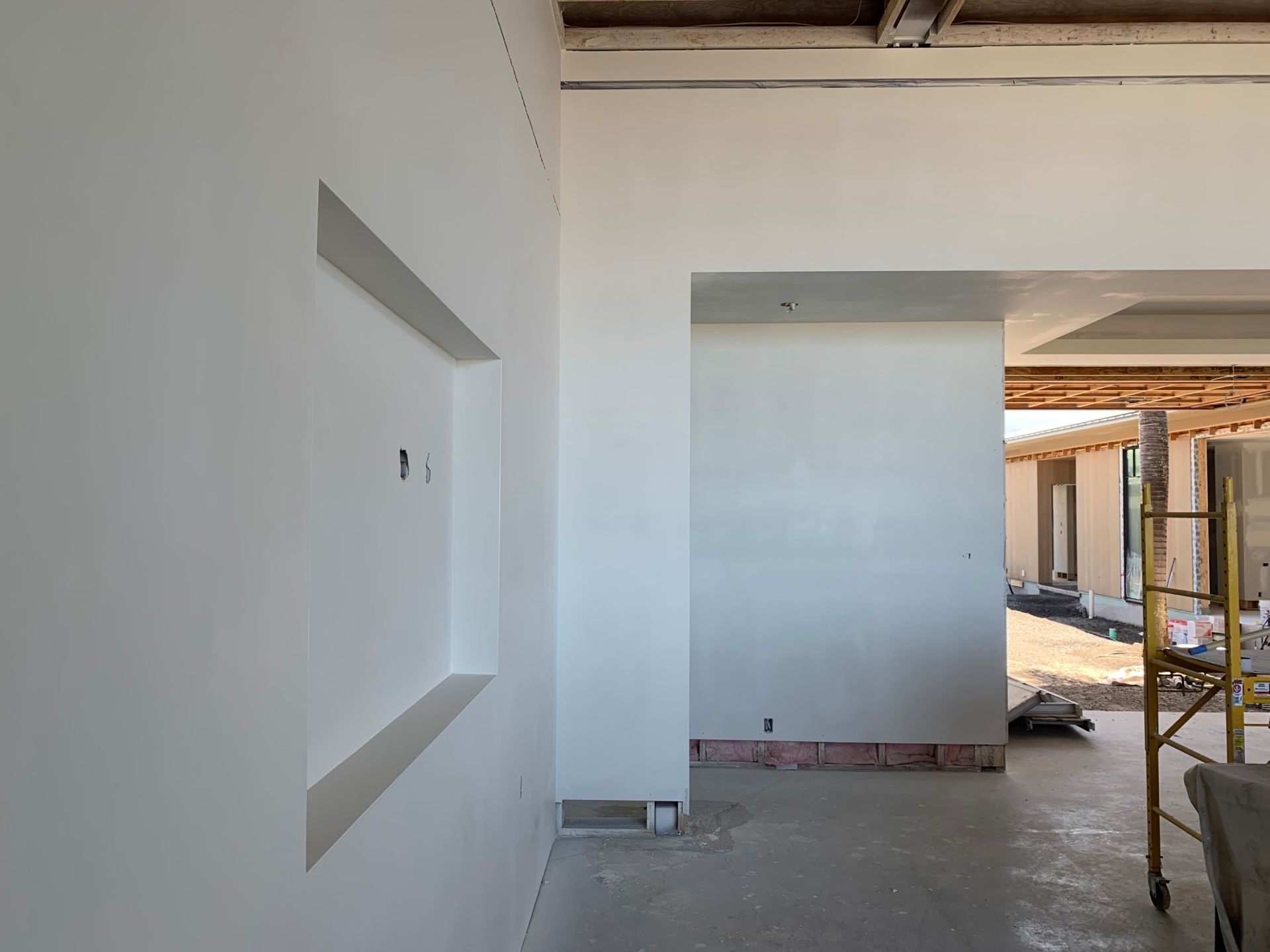 A building under construction with a scaffolding in the background and drywall installation finished.