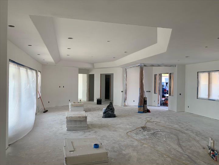 An empty room with white walls and a vacuum cleaner on the floor and just installed drywall.