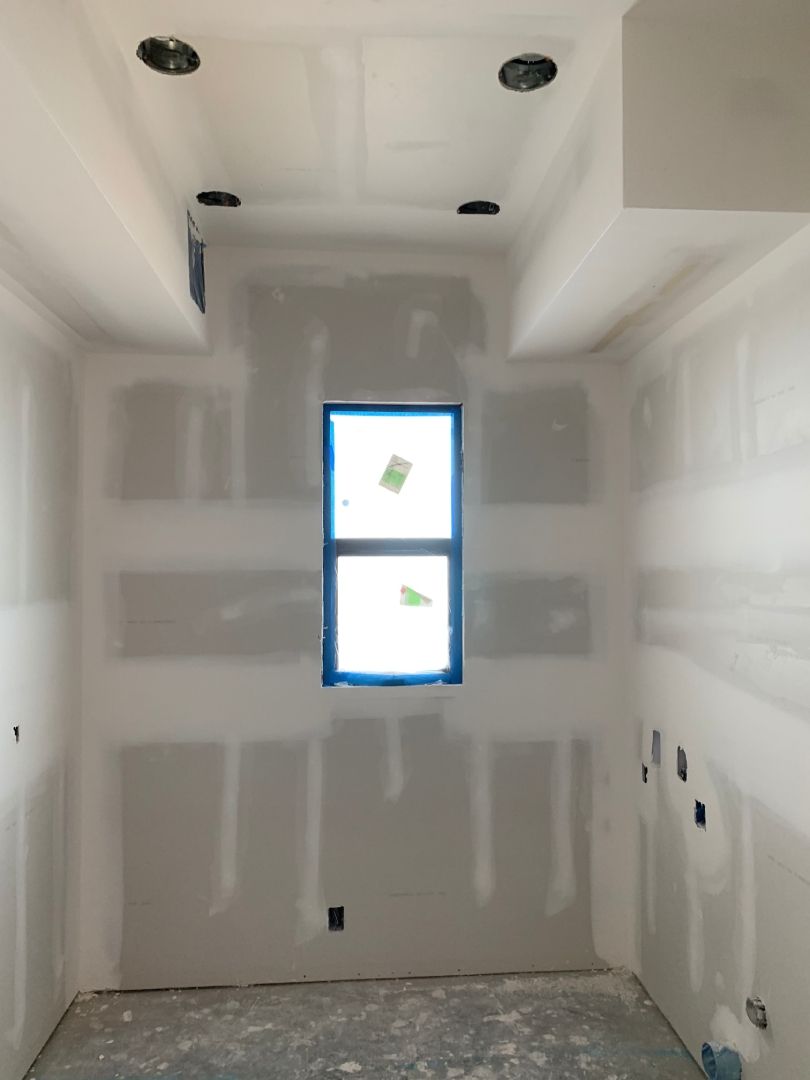 An empty room with a window in the middle of it and just completed drywall installation. 