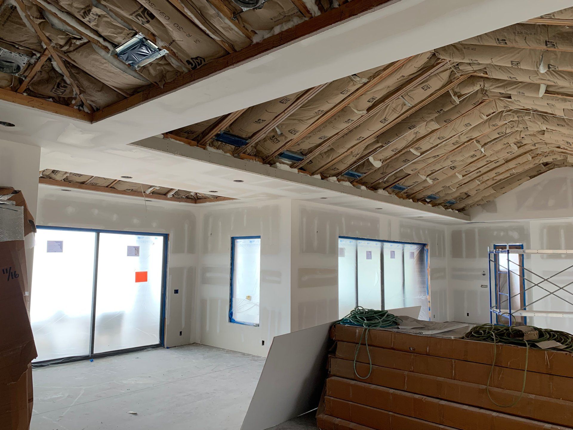 An empty room with a wooden ceiling and a lot of windows and drywall installed on the walls. 