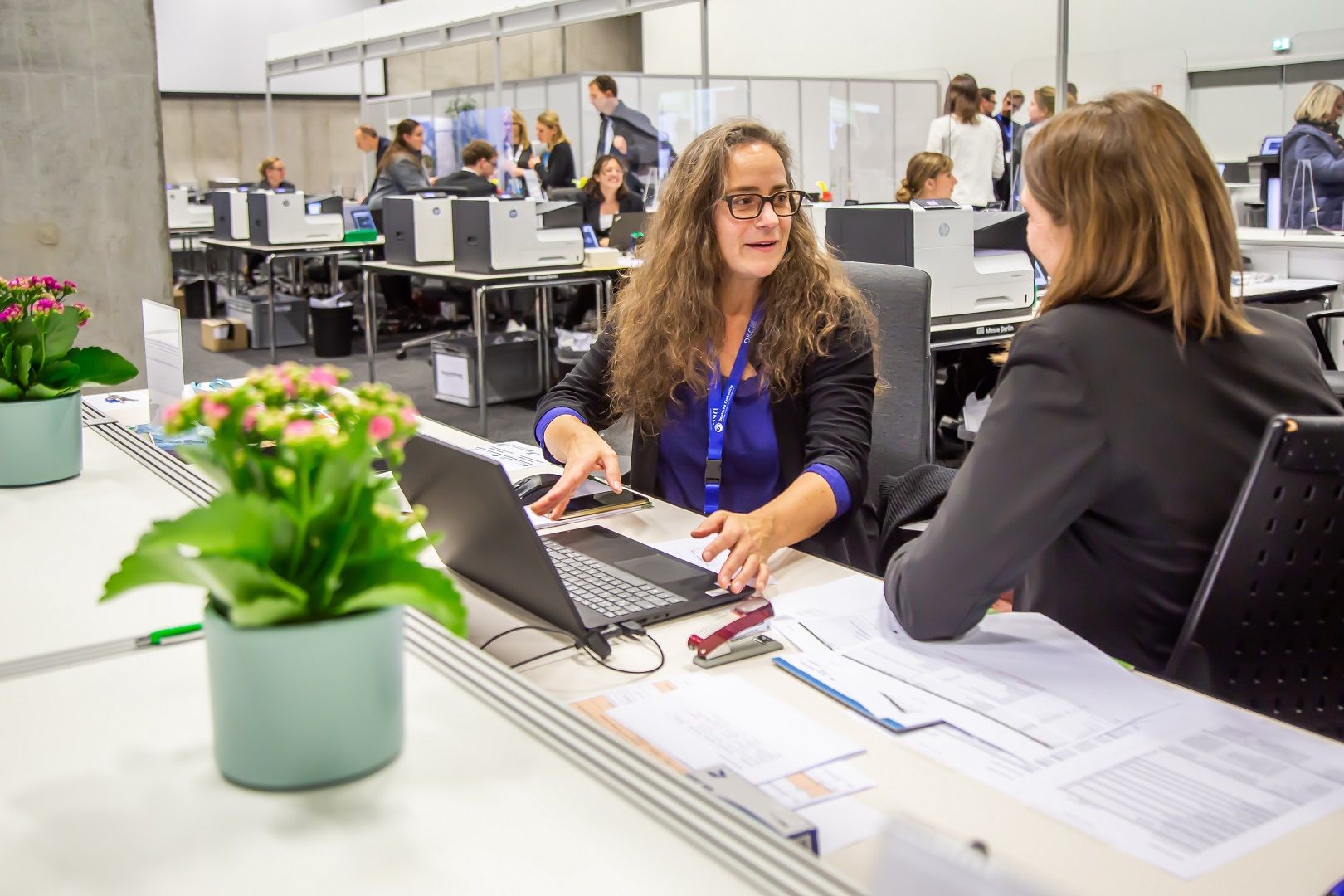 zwei Kolleginnen KUKM im Gespräch am Registrierungs-Counter vor Ort beim Deutschen Krebskongress 2024