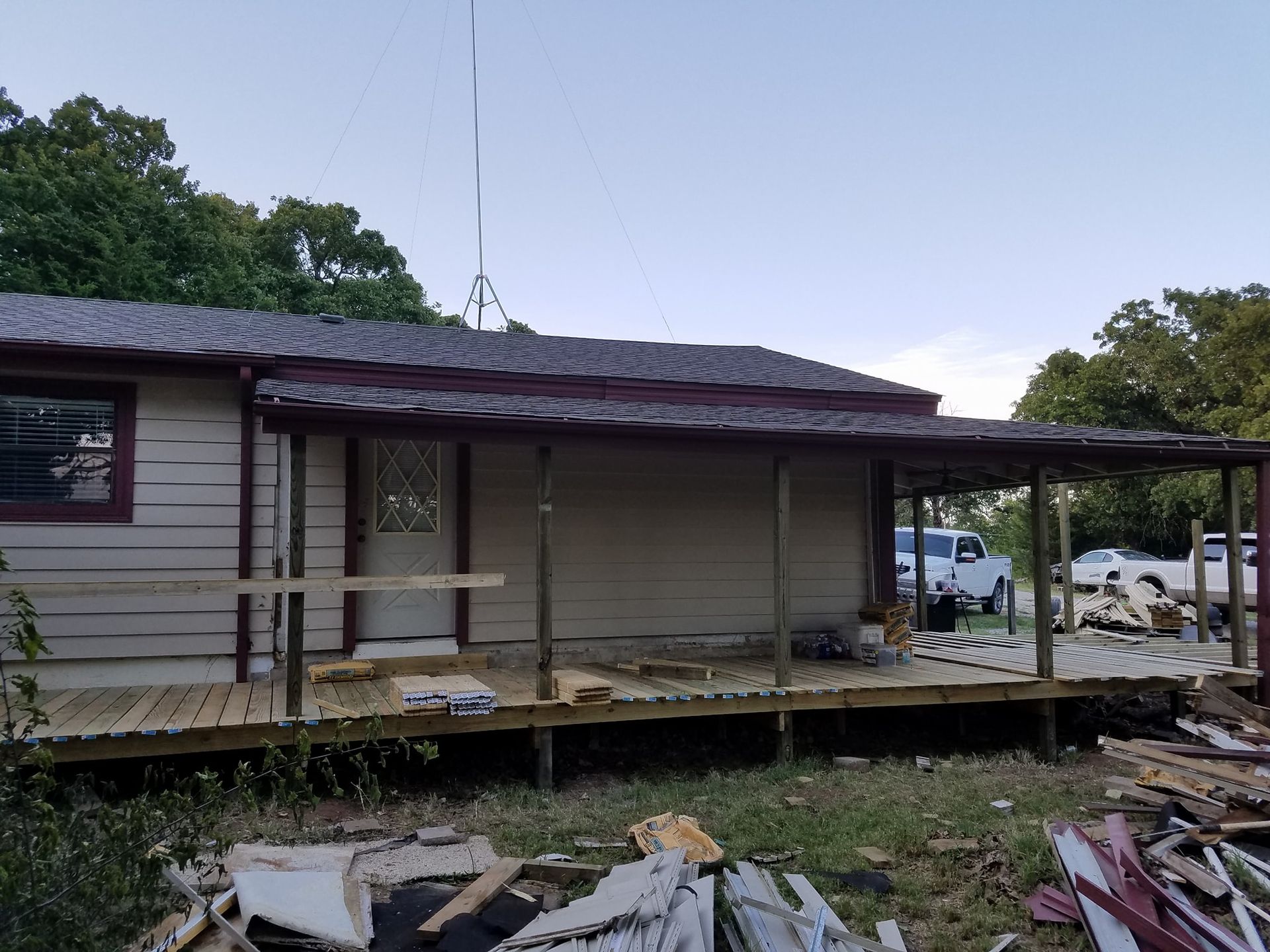 Dilapidated house with a damaged porch, debris in front, and trees in the background