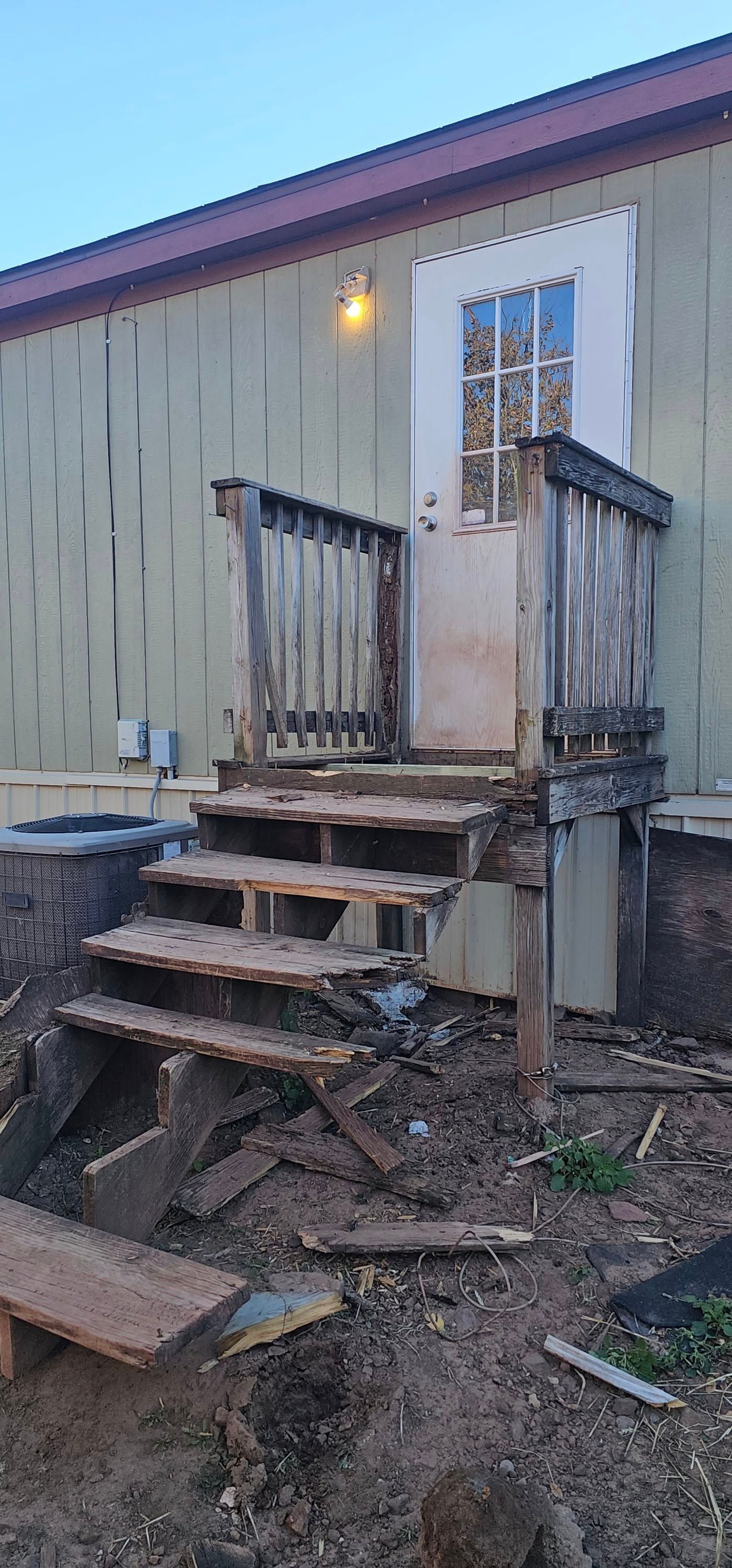 Weathered wooden steps leading to a door on a beige building, with a lit exterior light.
