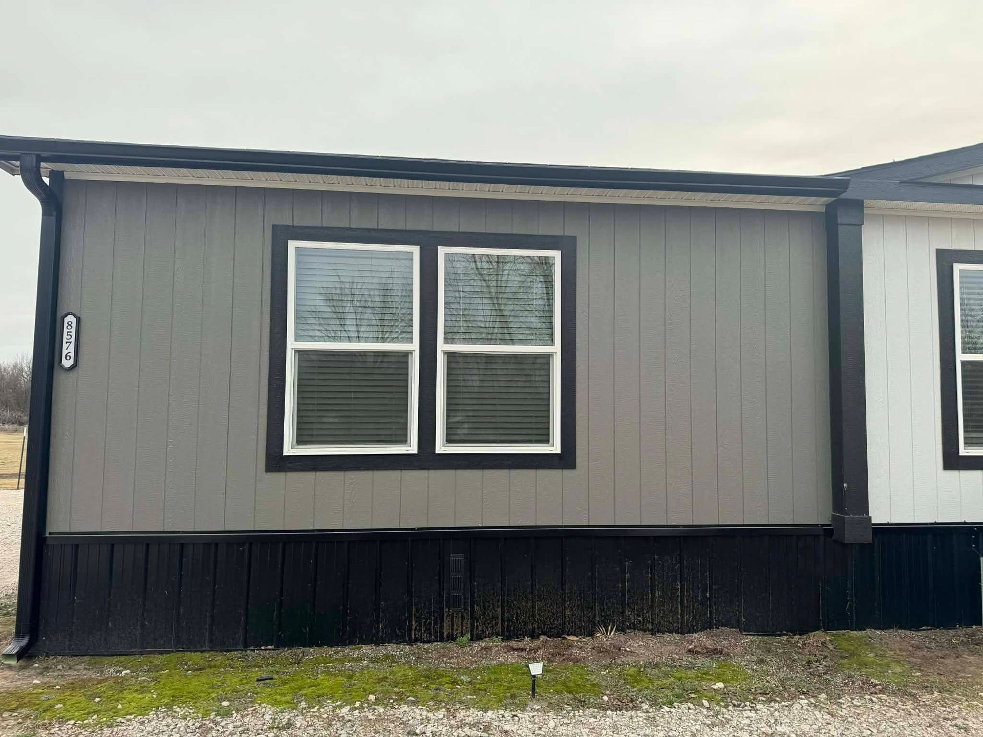 Exterior of a gray house wall with a double window and black lower siding under an overcast sky