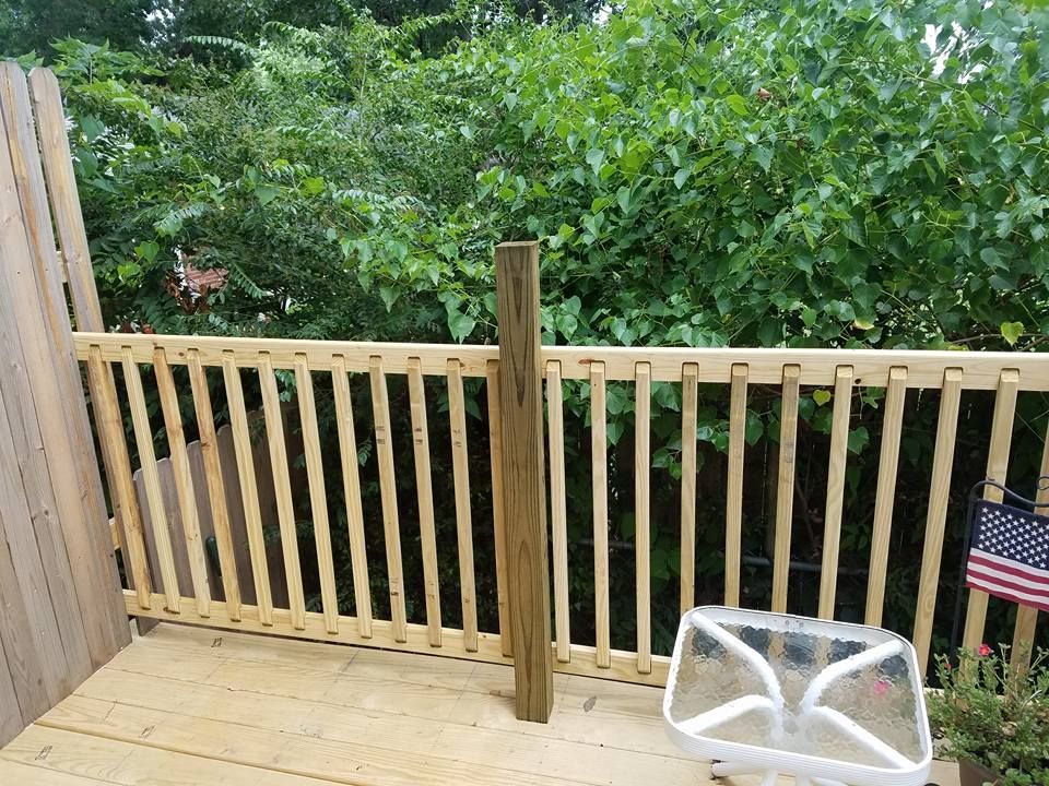 Wooden deck with railing overlooking dense green trees, with a white folding chair and small American flag.