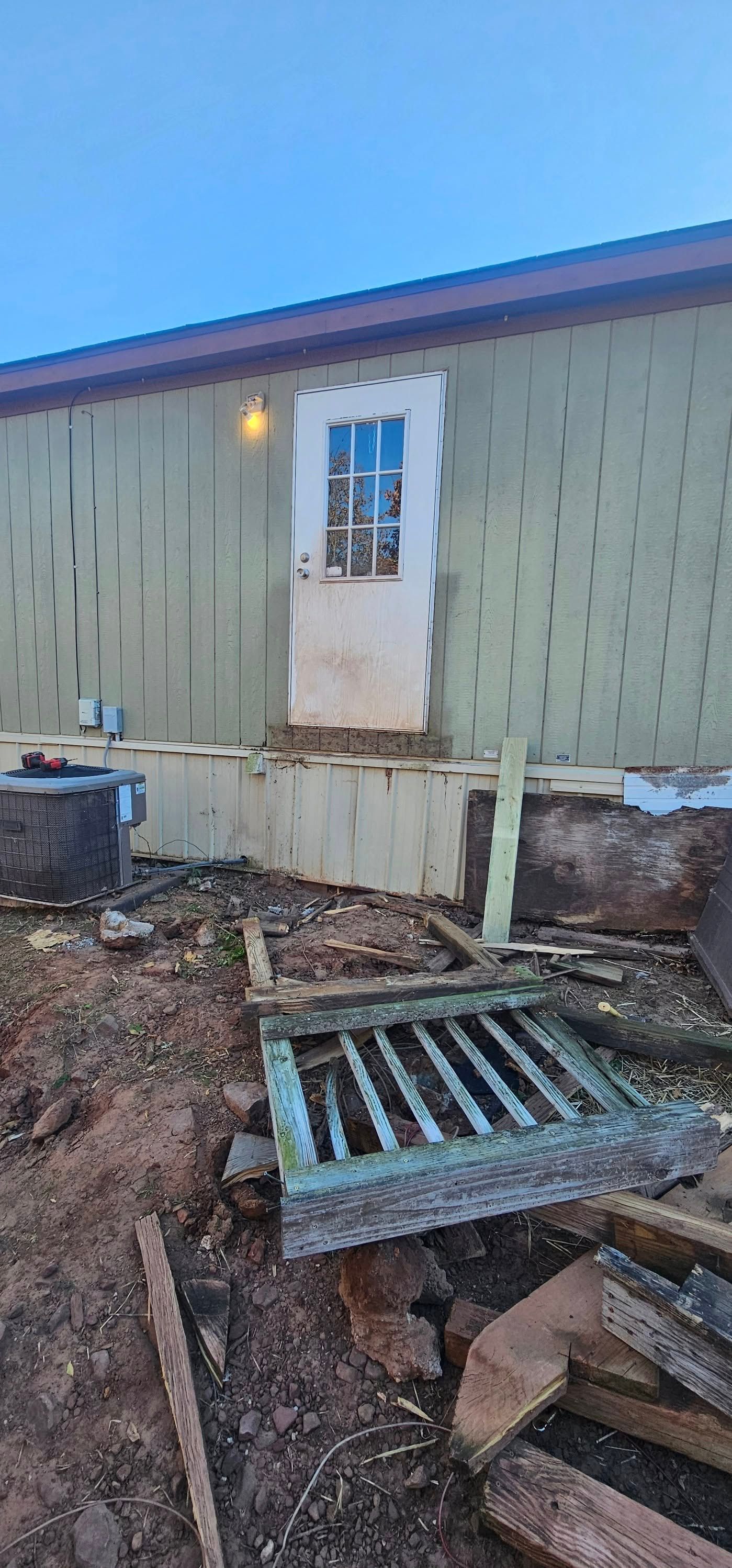 Damaged house exterior with broken steps and debris in the yard, viewed from the back door area