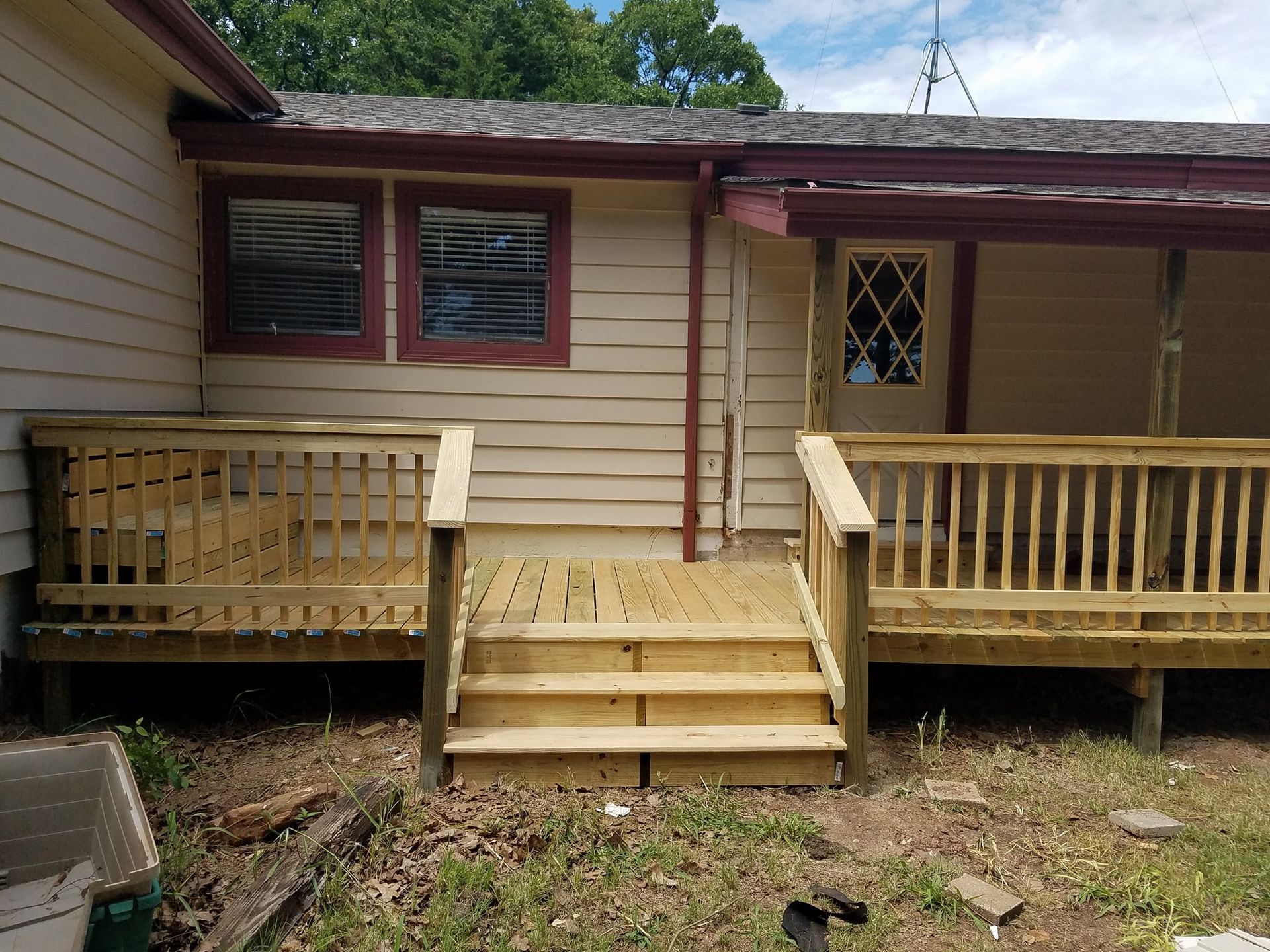 Front porch of a house with wooden steps and railings, beige siding, and a small deck under a maroon roof