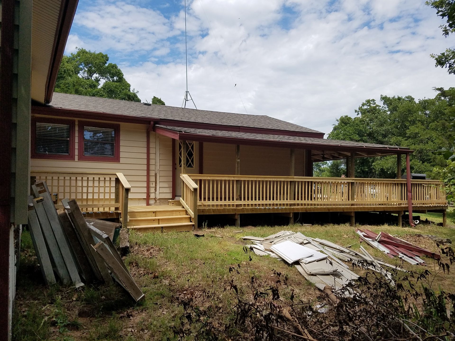 Weathered house with a wooden porch, debris in the yard, and trees in the background.
