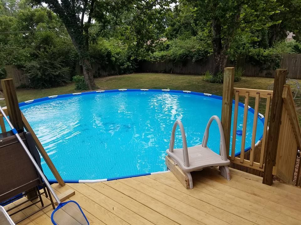 Backyard pool with blue water, wooden deck, and small diving board surrounded by trees