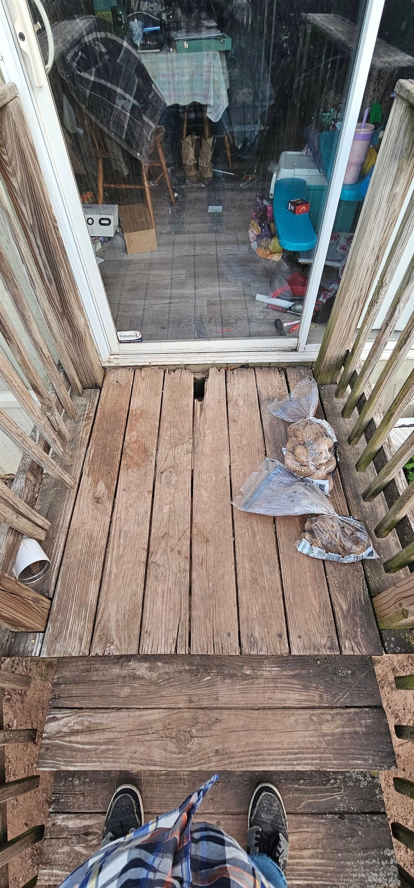 Looking down a narrow wooden stairway and dock toward a glass door, with tools and clutter on the sides.
