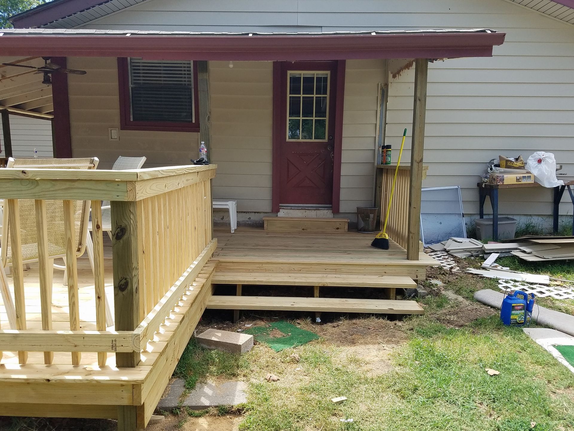 Front porch with wooden ramp, steps, red door, and beige siding on a small house