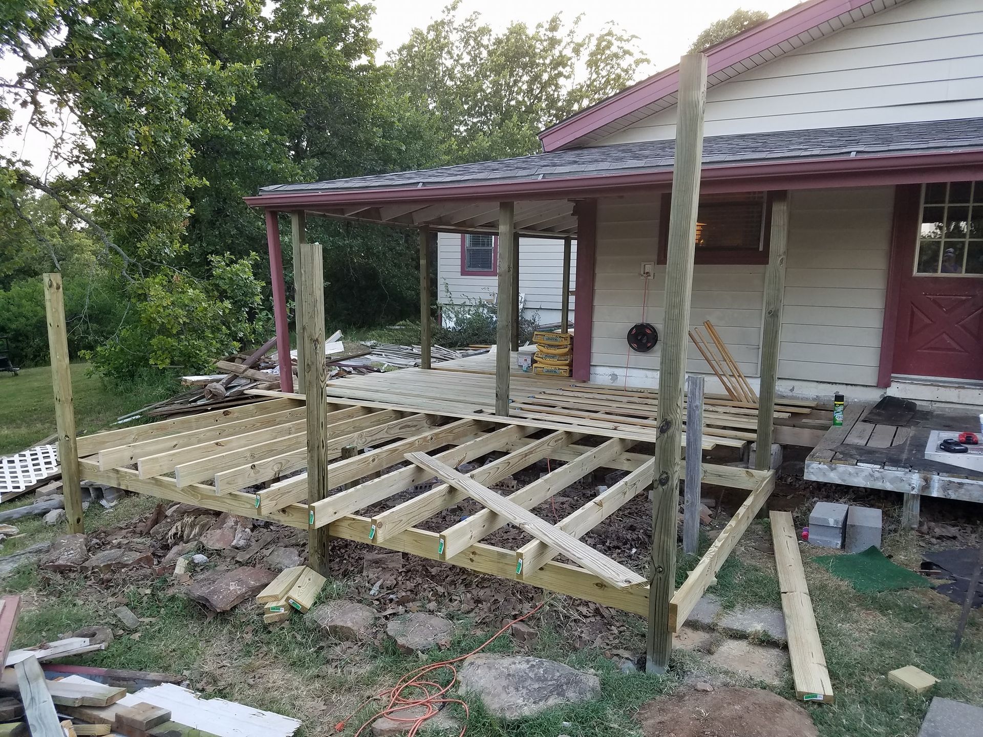 Partially built wooden porch ramp beside a house, with posts and joists exposed.