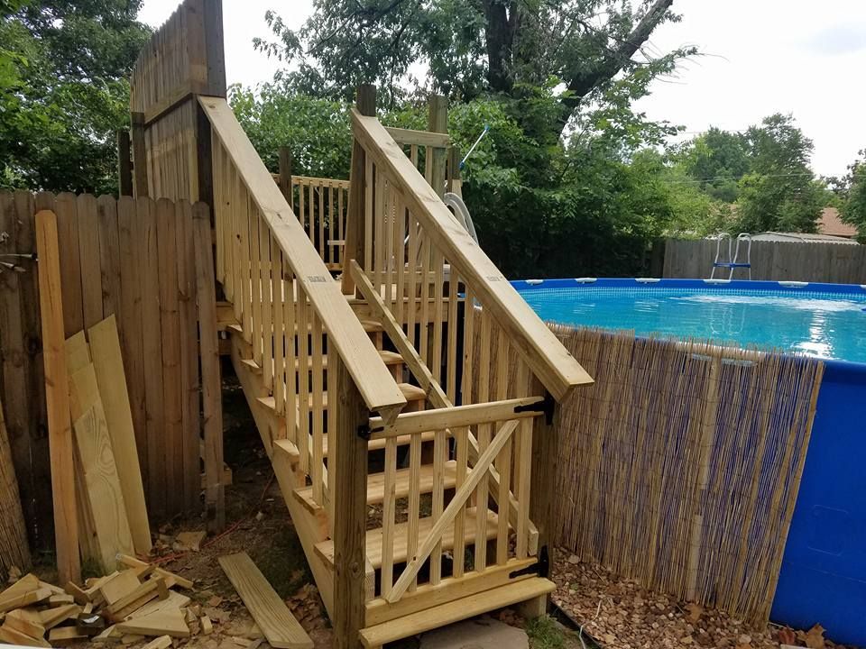 Wooden backyard staircase and railing beside a blue above-ground pool and fence
