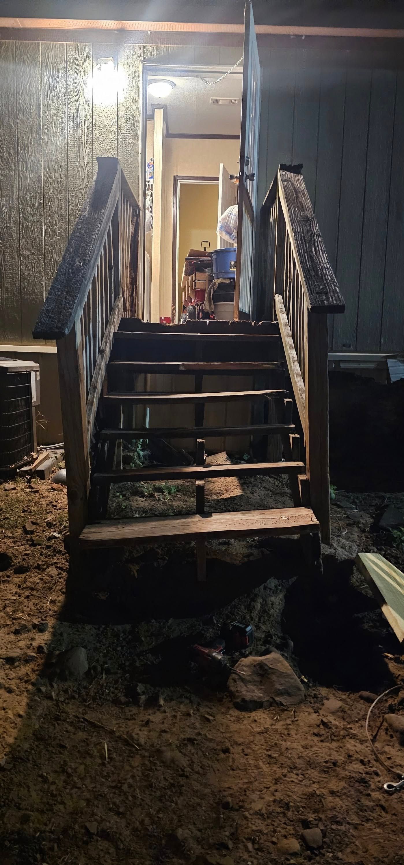 Dimly lit front steps with rusty railings leading up to a doorway at night.