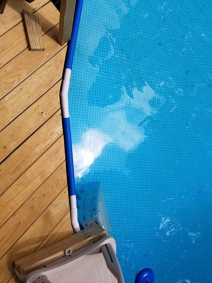 Blue pool edge with ladder on wooden deck, water splashing near the side.