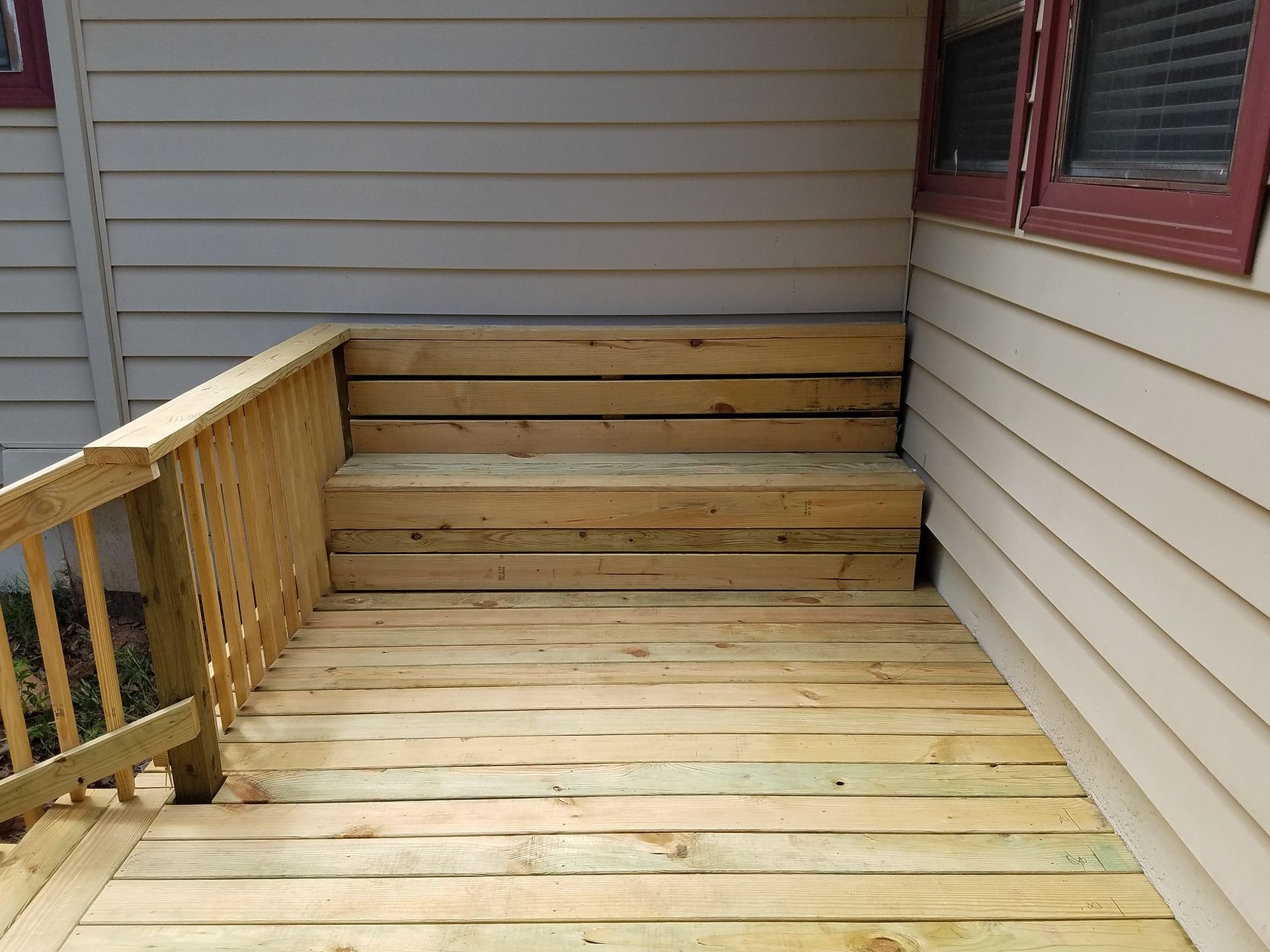 Wooden deck with steps beside a house, bordered by a railing and beige siding
