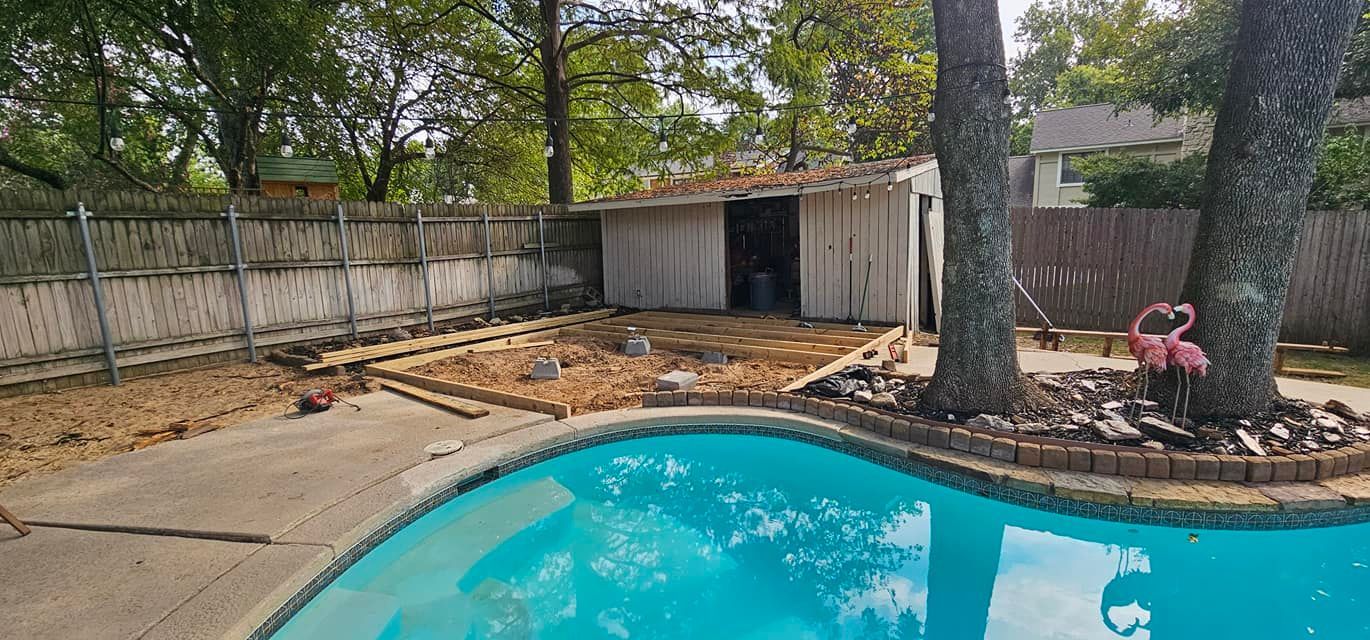 Backyard pool with a curved blue edge, trees, a shed, and a fenced dirt area with a red toy