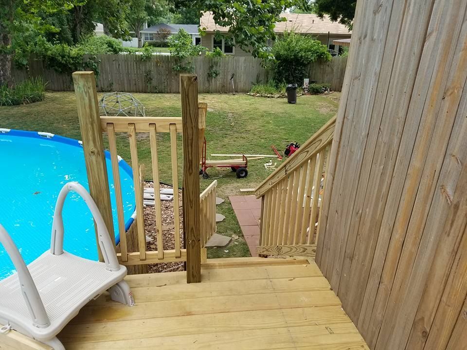 Backyard deck with stairs beside a blue pool and a fenced lawn beyond