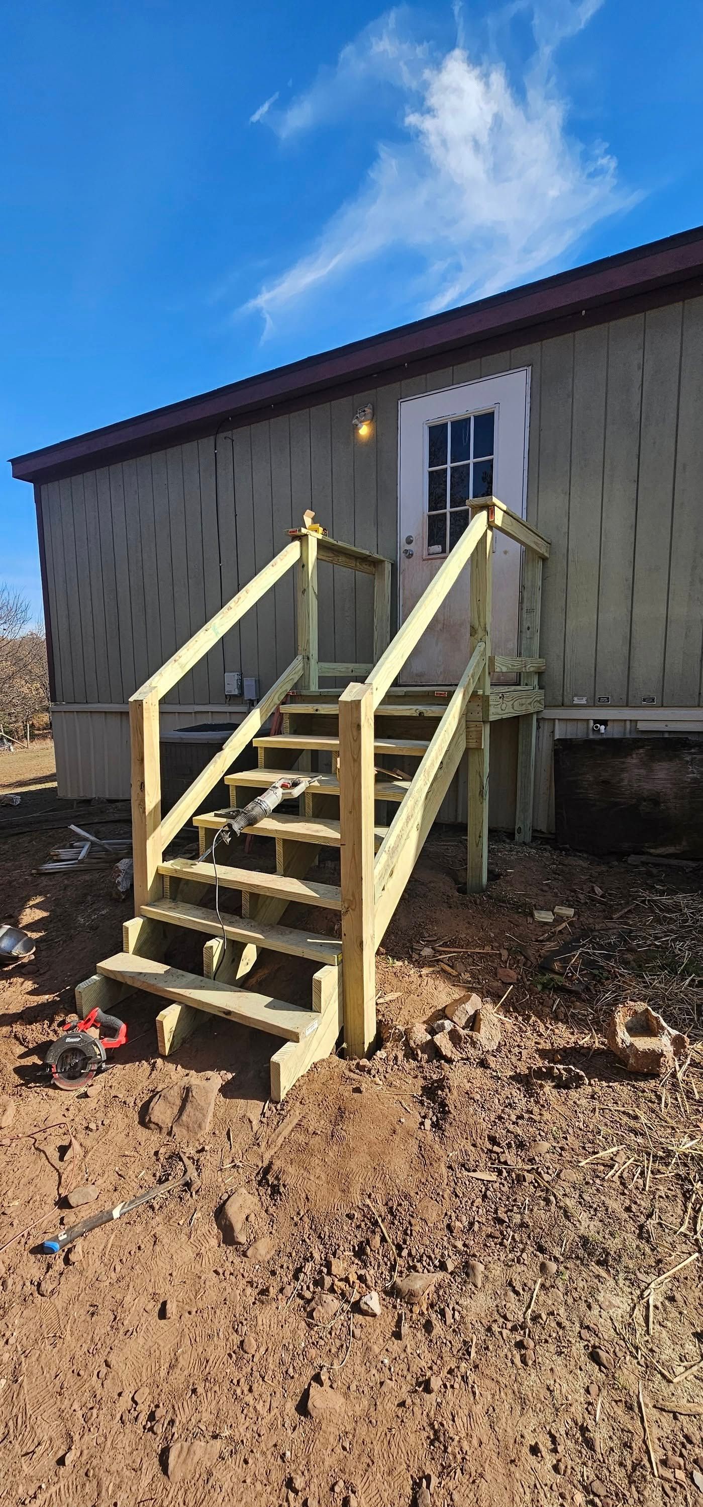 Wooden stairs with handrails leading to a white door on a small elevated building under a blue sky.