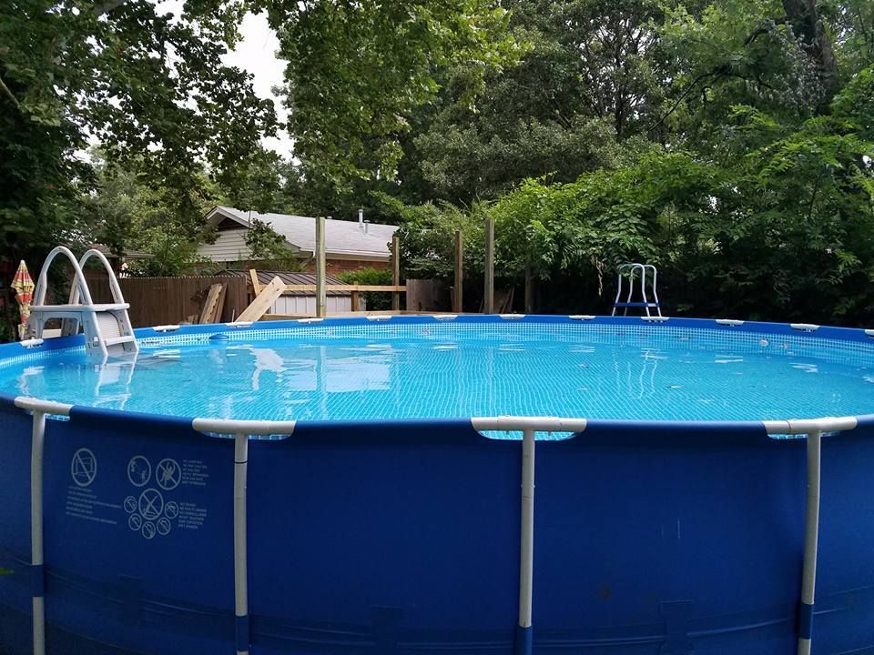 Above-ground backyard pool with blue water, ladder, and surrounding trees and patio furniture