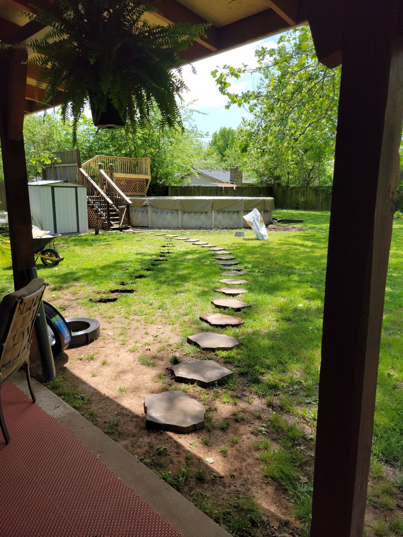Backyard patio view with stepping stones, grass, a small staircase, and a white chair near trees and a fence
