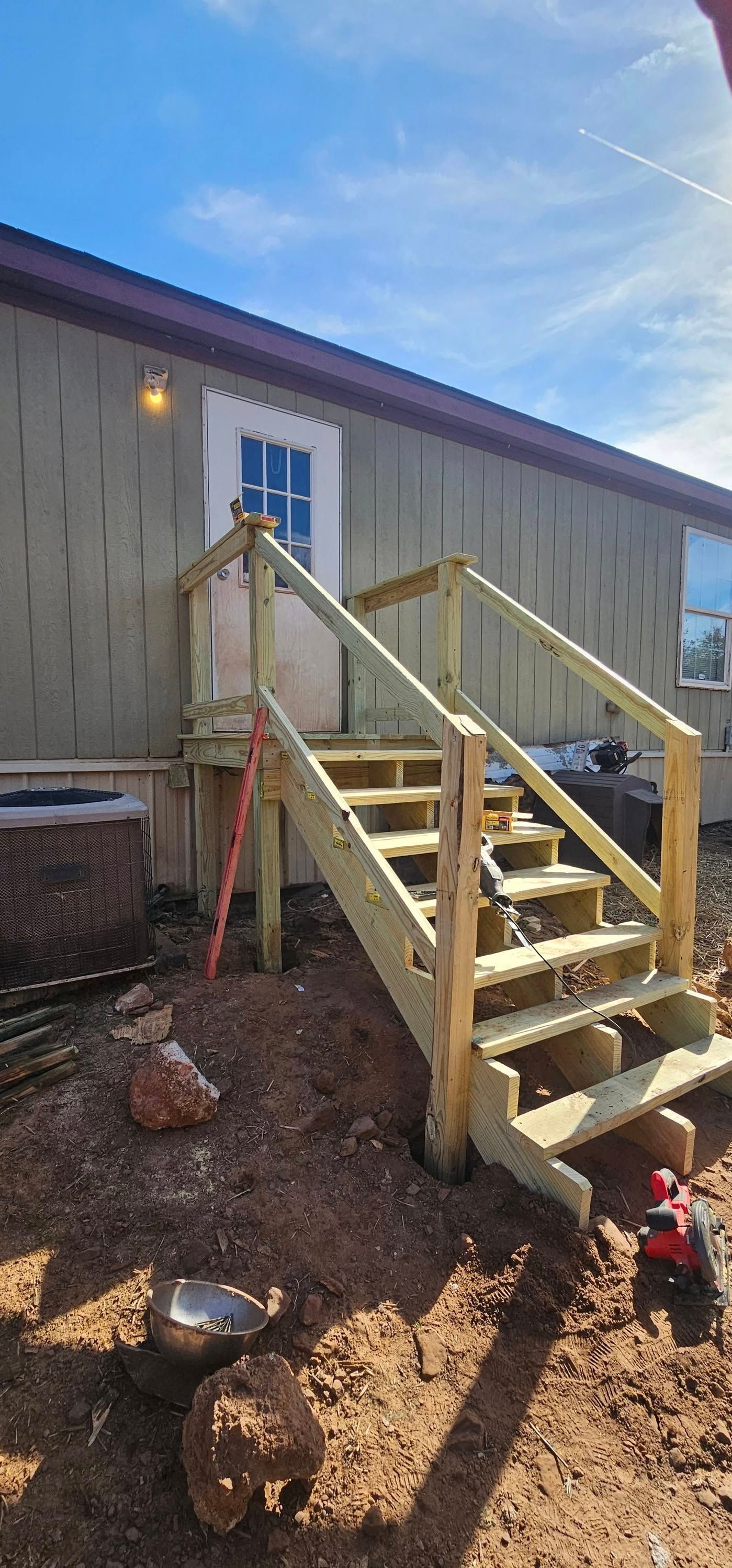Exterior stairs leading to a white door on a tan building, with wooden railings and dirt ground.