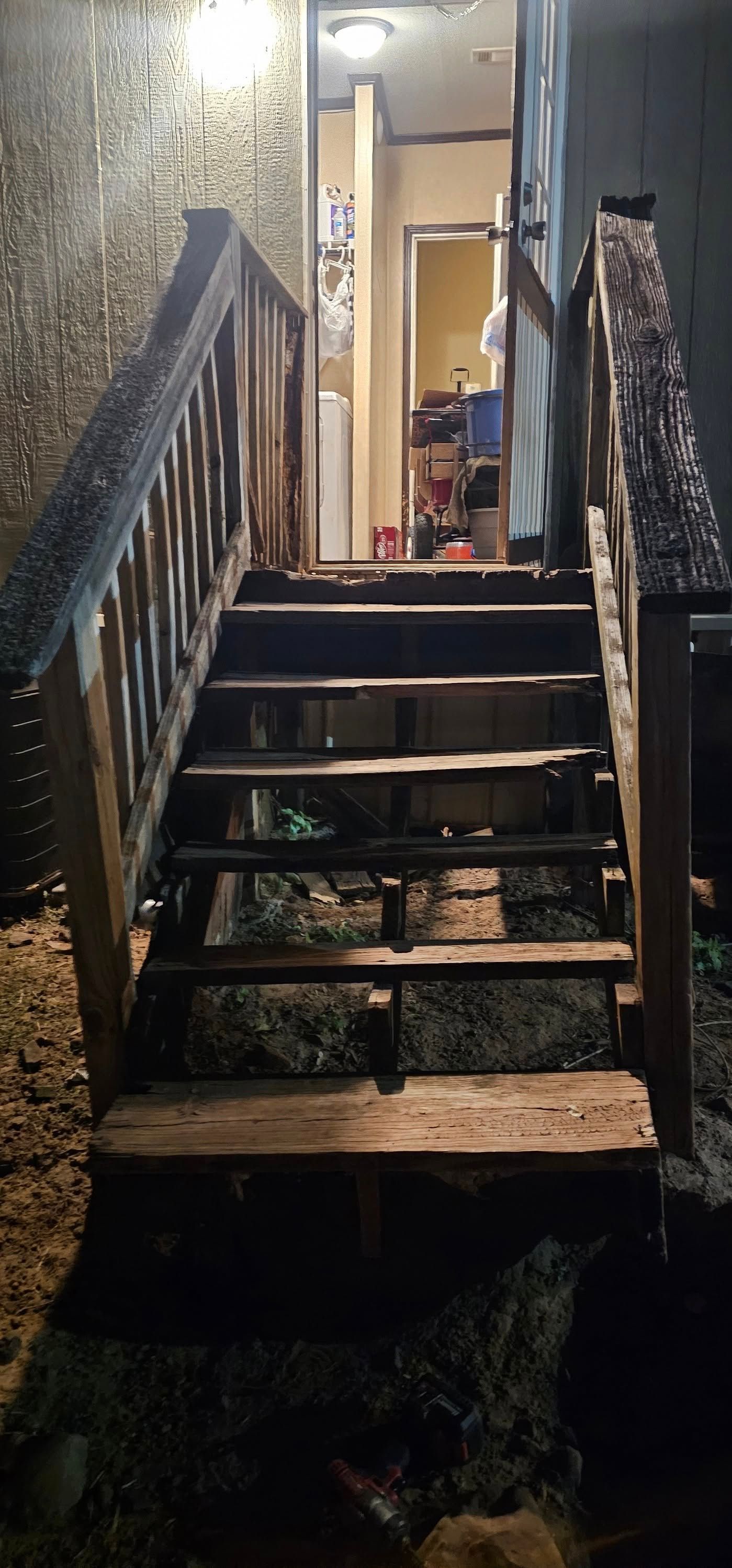 Narrow outdoor wooden stairs leading up to a lit doorway at night