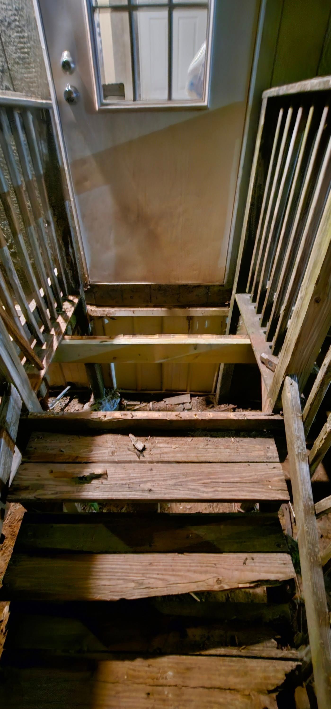 Broken wooden stairs in a dim stairwell with a window at the top