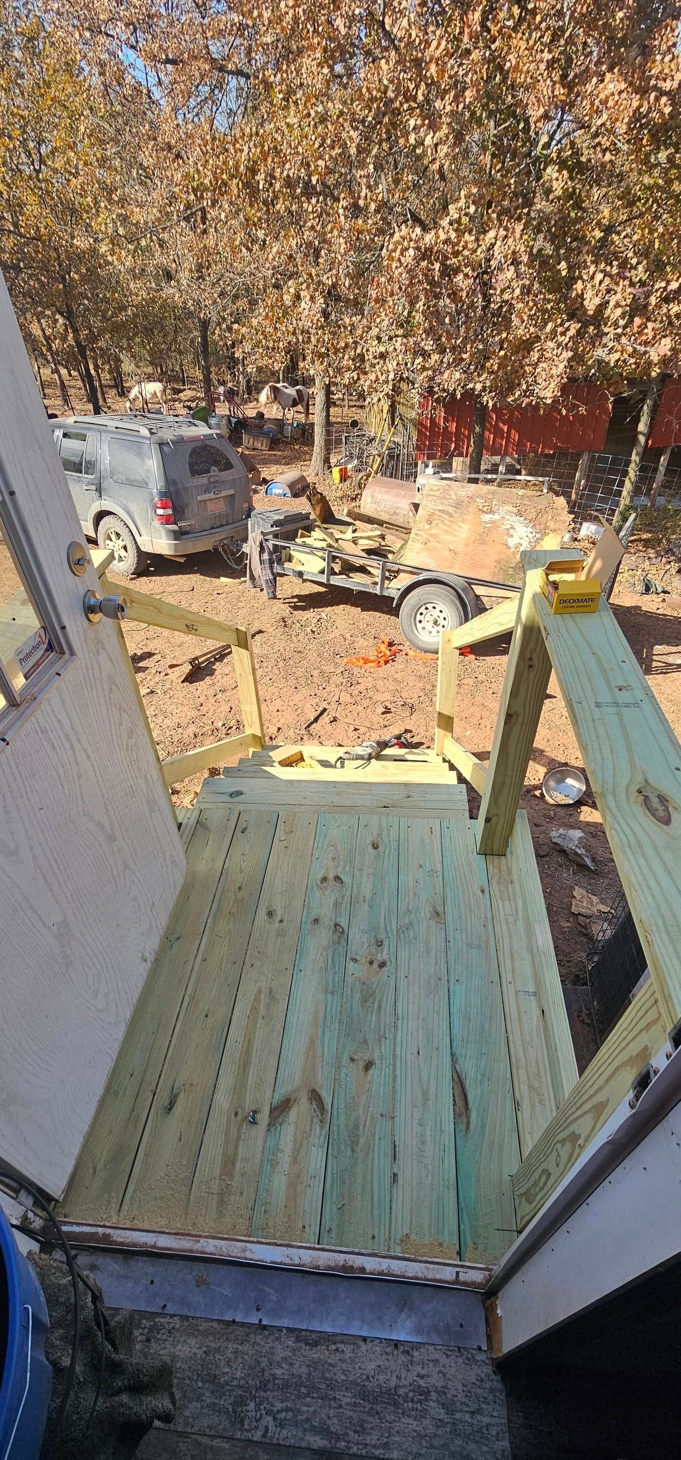 Front porch with teal steps overlooking a leaf-covered yard and parked cars in autumn.